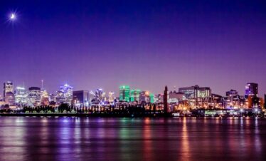 A stunning nighttime view of Montreal's skyline reflecting on the St. Lawrence River under a crescent moon.