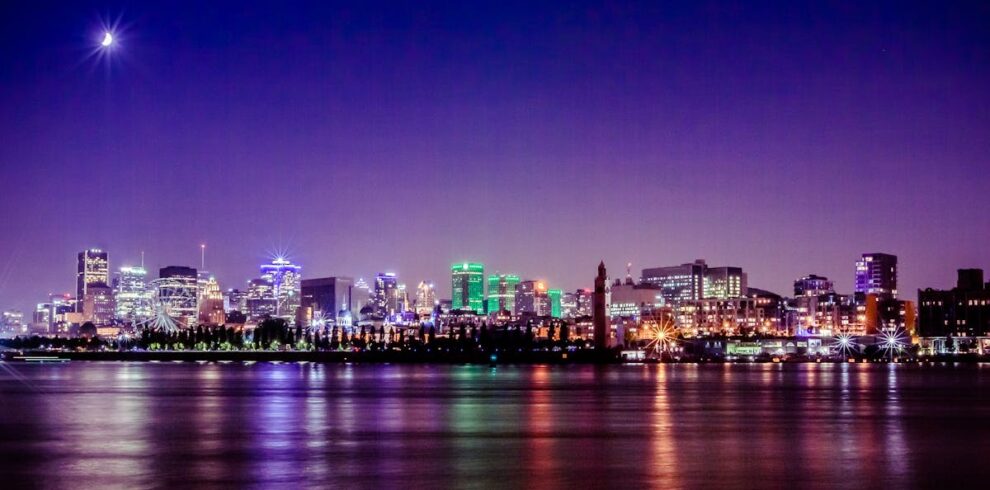 A stunning nighttime view of Montreal's skyline reflecting on the St. Lawrence River under a crescent moon.